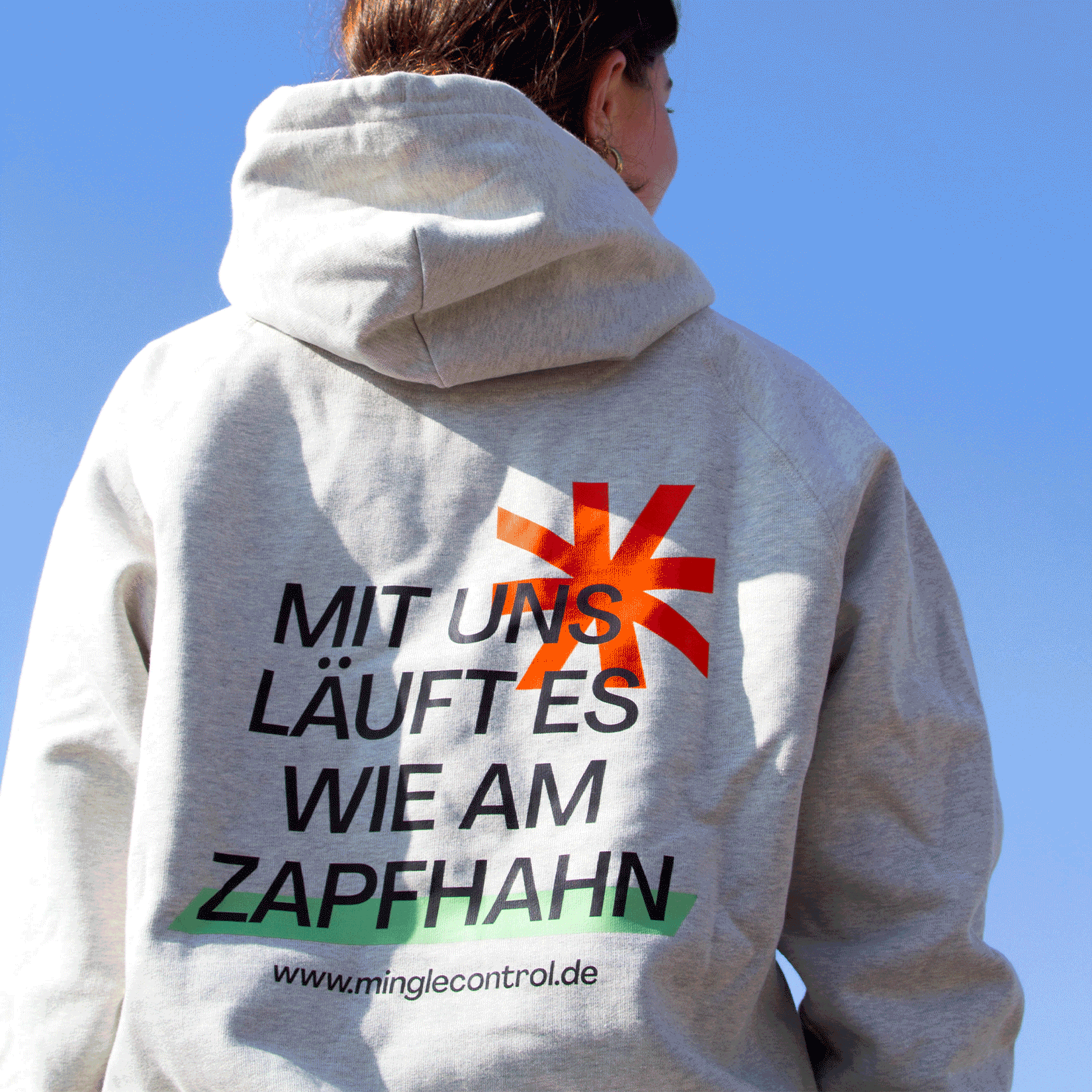 Frau trägt einen grauen Hoodie mit backprint. Darauf steht der claim "Mit uns läuft es wie am Zapfhahn" sowie der Link zur Webseite von MINGLECONTROL